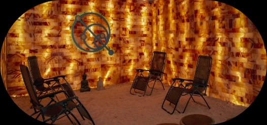 A salt therapy room with illuminated orange salt brick walls, four reclining chairs on a salt floor, and two small Buddha statues.