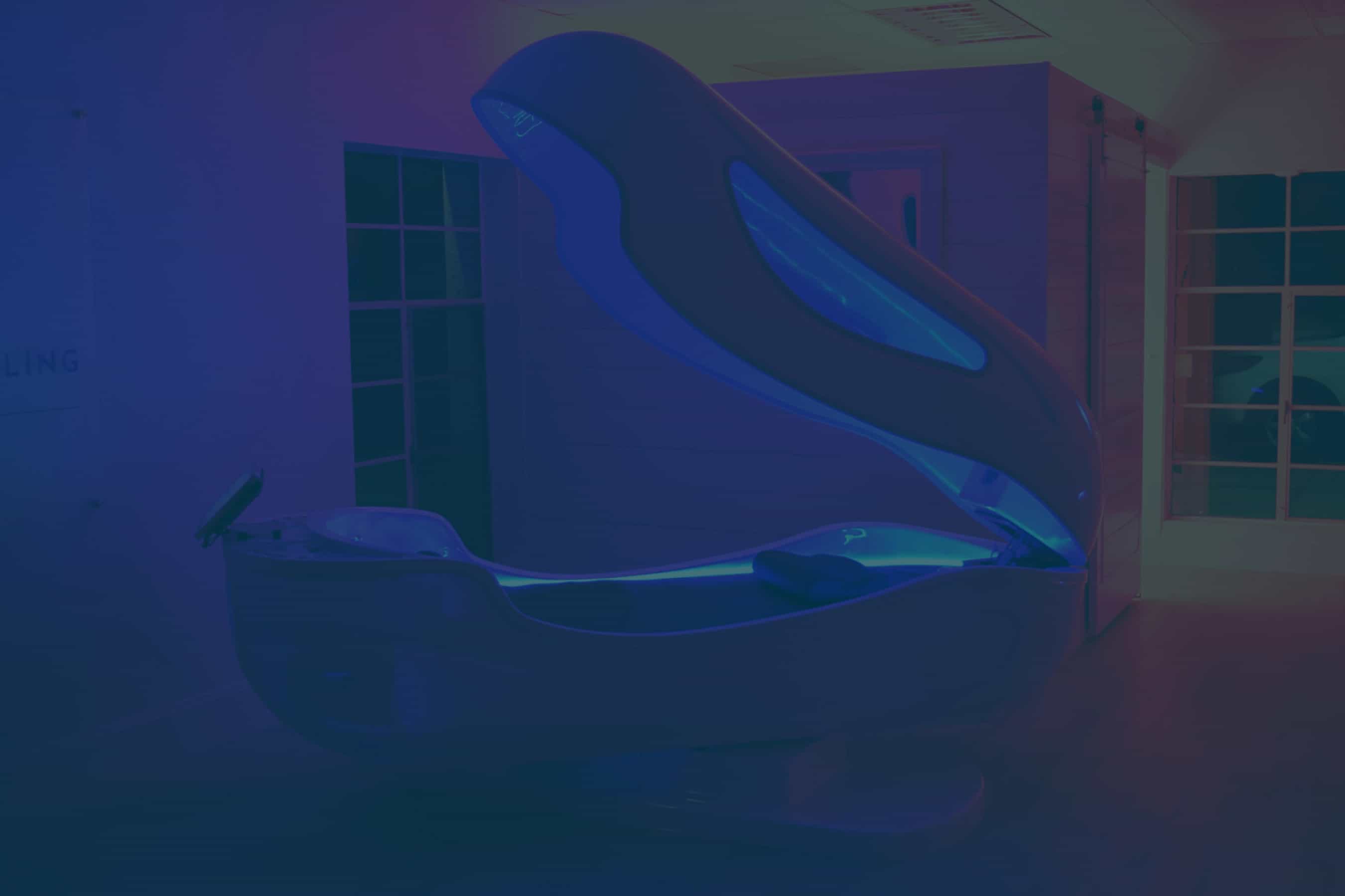 An open, futuristic floatation therapy pod glowing with blue light in a dark, serene room.