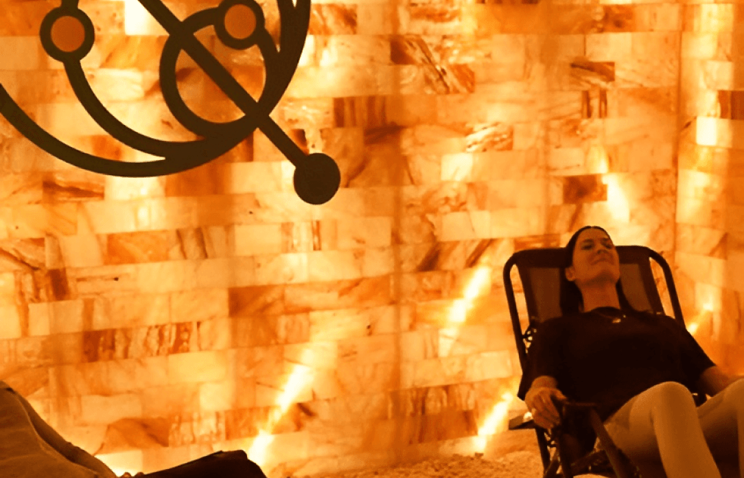 Woman relaxing in a salt therapy room with glowing orange salt brick walls and a dark metal decoration.